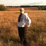 Person with a baseball hat and white sweatshirt standing in a field