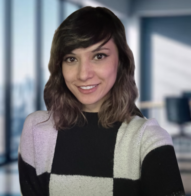 Person with medium brown hair wearing a sweater with white, pink, and black squares smiles directly to the camera
