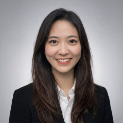 Person with long brown hair and wearing a black suit top with a white shirt smiles directly at the camera